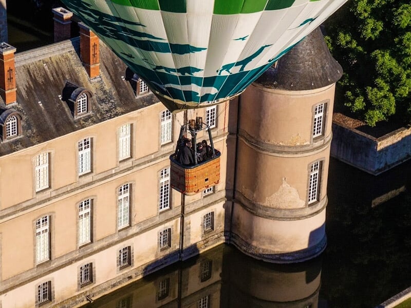 Gros plan sur une montgolfière au-dessus d'un château avec reflet dans l'eau.