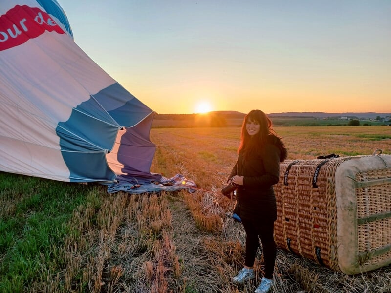 Une femme debout près d'une montgolfière en train de se gonfler au lever du soleil dans un champ à Lunéville.