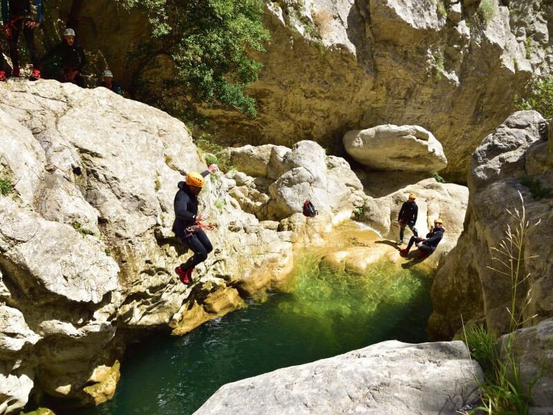 Personne sautant dans une eau claire entourée de rochers lors d'une activité de canyoning en pleine nature.