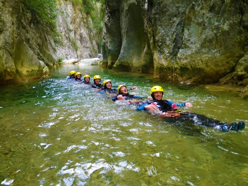 Groupe de participants en ligne flottant sur le dos dans une rivière claire lors d'une sortie canyoning.