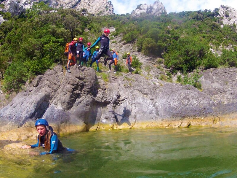Personnes sautant dans une eau verte depuis un rocher lors d'une aventure canyoning en plein air.