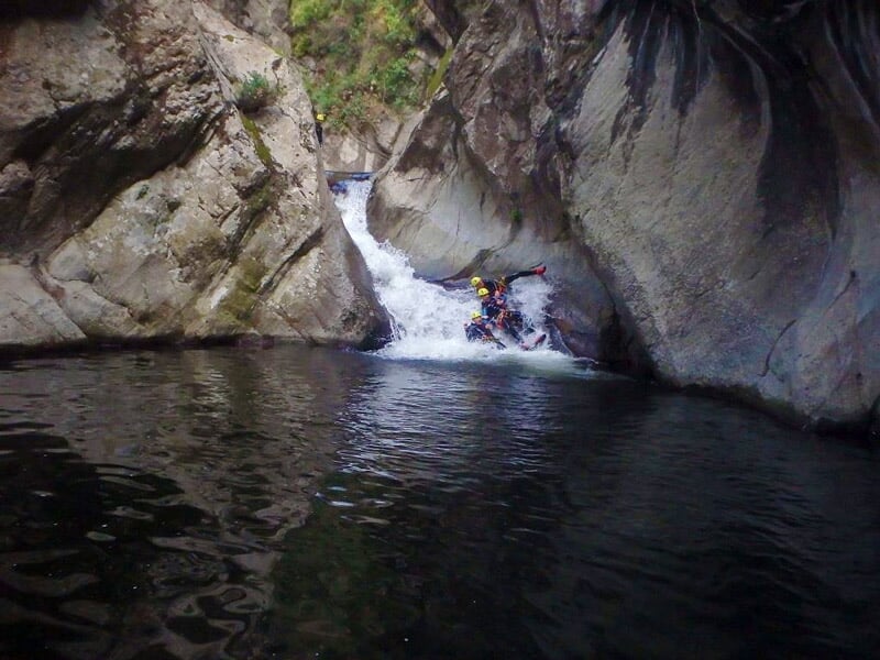 Deux personnes en combinaison et casque glissent dans un toboggan naturel d'eau dans un canyon rocheux.