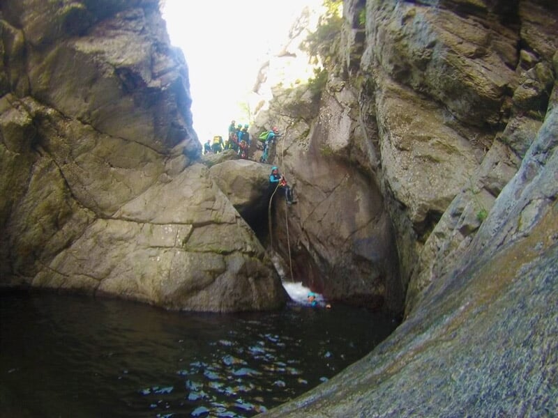 Groupe de personnes en haut d'une falaise rocheuse préparant une descente en rappel dans un canyon.