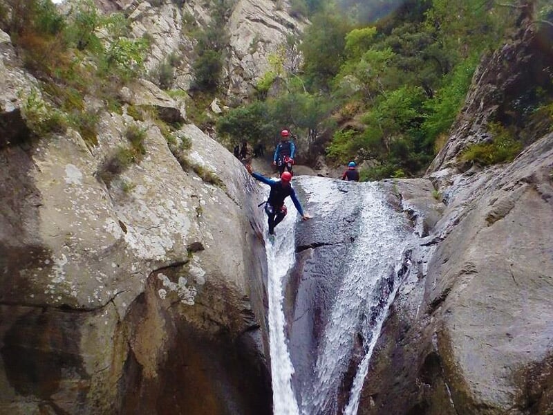 Personne en combinaison et casque rouge saute d'une falaise rocheuse dans un bassin d'eau en canyoning.