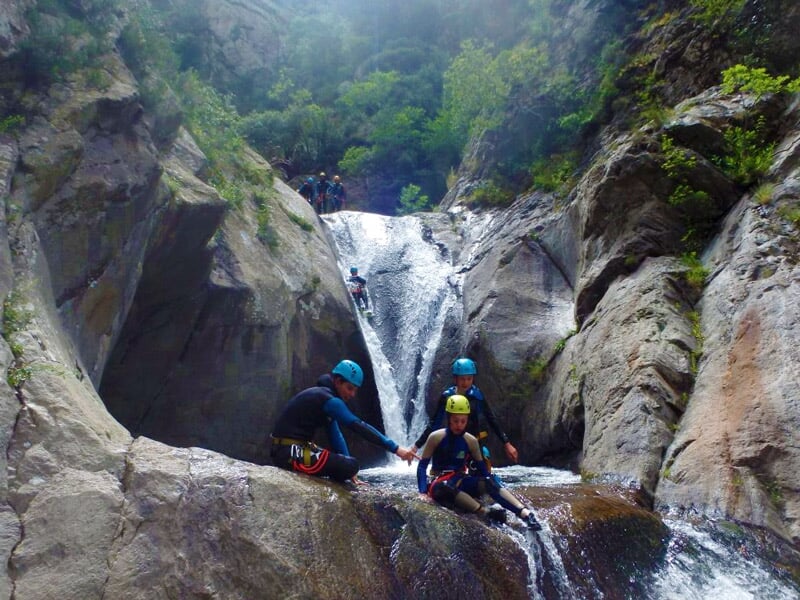 Groupe de personnes en casque bleu et jaune assis sur des rochers au bord d'une cascade en canyoning.