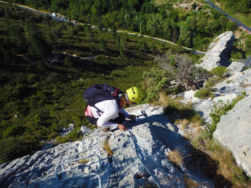 Femme en casque jaune grimpe une paroi rocheuse abrupte équipée d'une via ferrata en pleine nature.