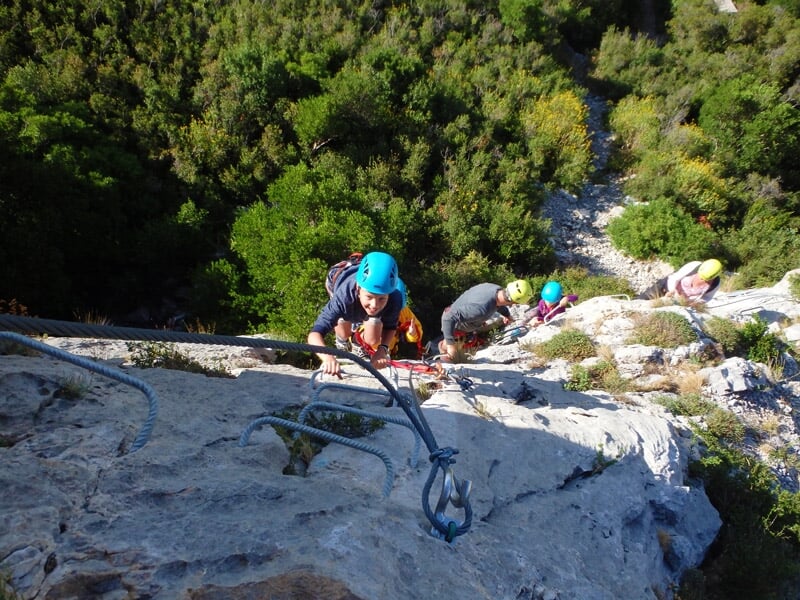 Groupe de personnes en casque bleu et jaune escaladent une paroi rocheuse équipée d'une via ferrata.