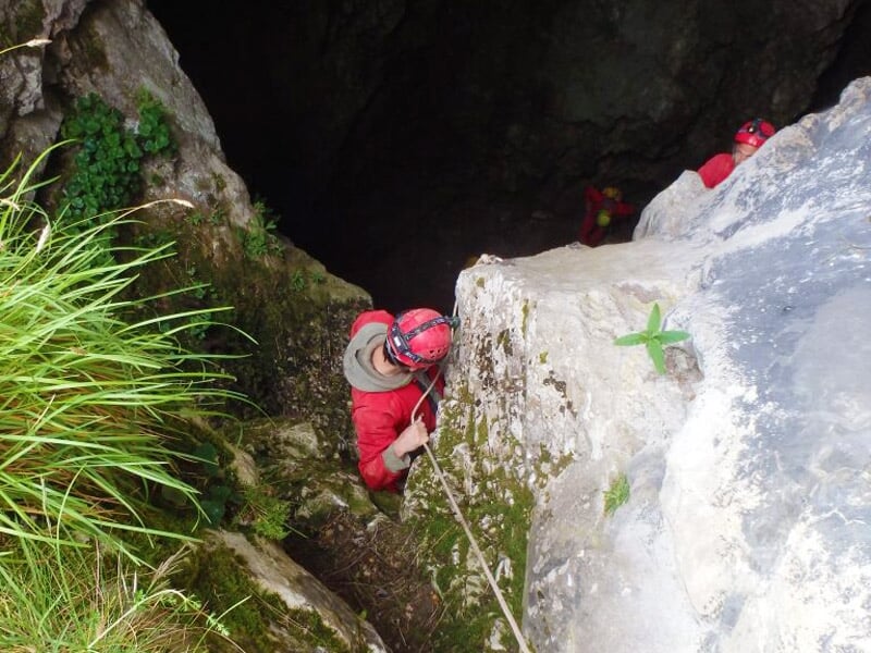 Deux spéléologues en combinaison rouge progressent dans une cavité rocheuse étroite et humide.