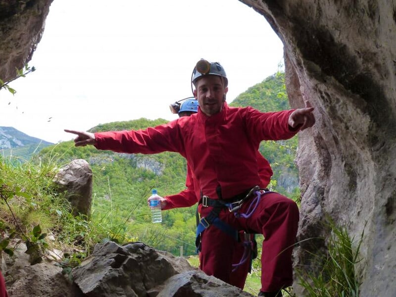 Spéléologue en combinaison rouge descend en rappel dans une cavité rocheuse étroite et humide.