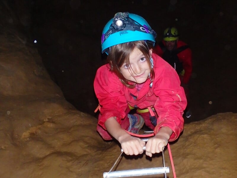 Groupe de spéléologues en combinaison rouge posant dans une cavité rocheuse avec stalactites.