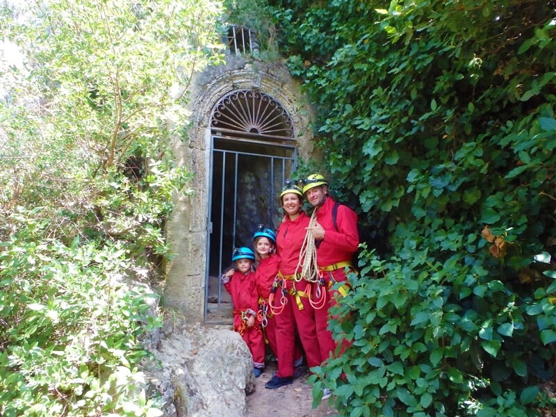 Enfant en combinaison rouge explorant une cavité rocheuse étroite avec lampe frontale.