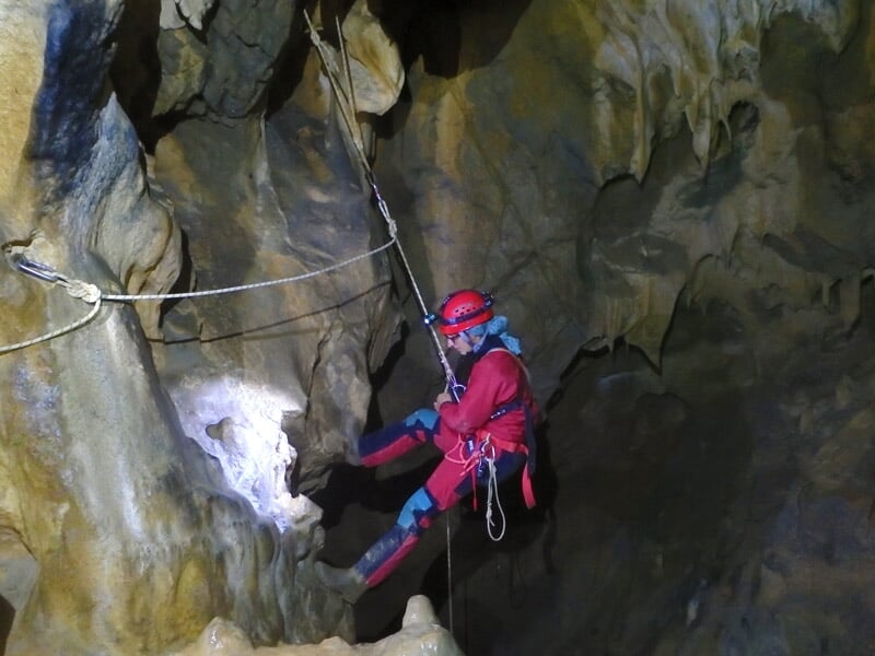 Enfant en combinaison noire explorant une cavité rocheuse étroite avec lampe frontale.
