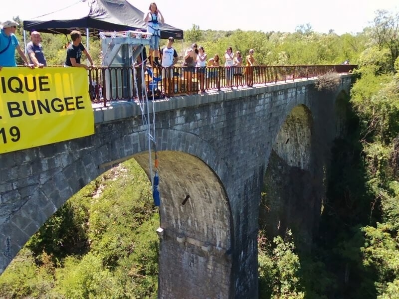 Groupe de personnes sur un pont en pierre observant un saut à l'élastique en cours.