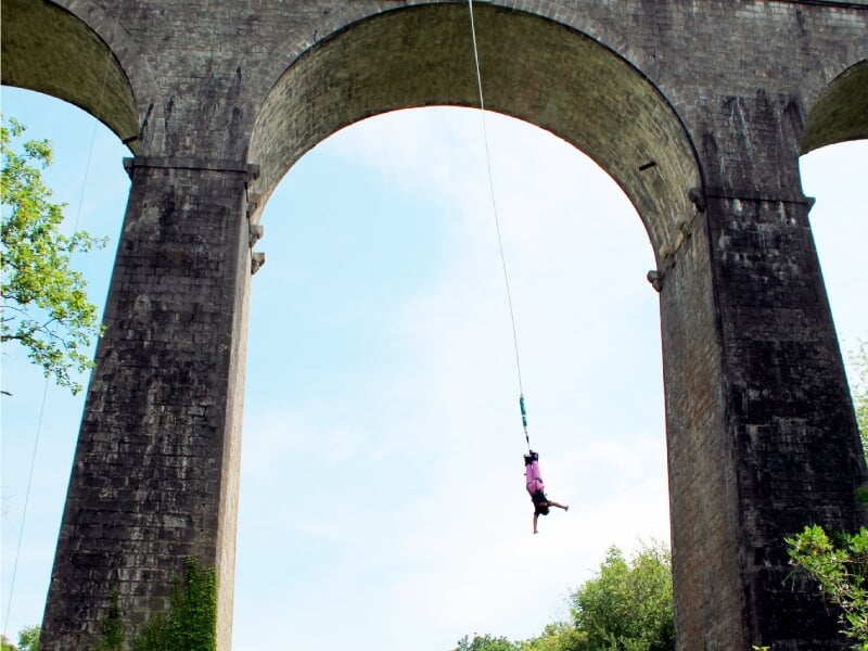 Personne suspendue en plein saut à l'élastique sous un grand arc de pierre d'un viaduc.