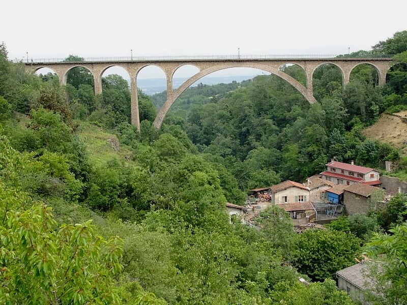 Viaduc en béton surplombant un village entouré de collines et de végétation dense.