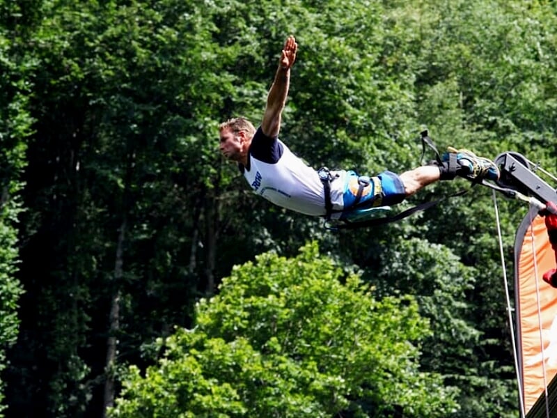 Homme en saut à l'élastique avec les bras écartés au-dessus d'une forêt verdoyante.