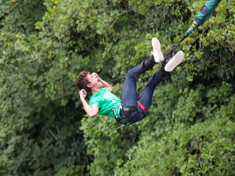 Jeune homme en saut à l'élastique avec expression de joie, suspendu au-dessus des arbres.
