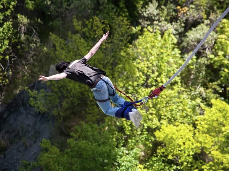 Femme en saut à l'élastique avec les bras ouverts, suspendue au-dessus d'une végétation dense.