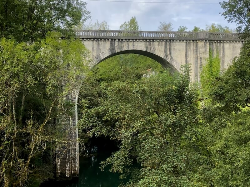 Viaduc en pierre entouré d'arbres verts avec une rivière en contrebas visible à travers les arches.
