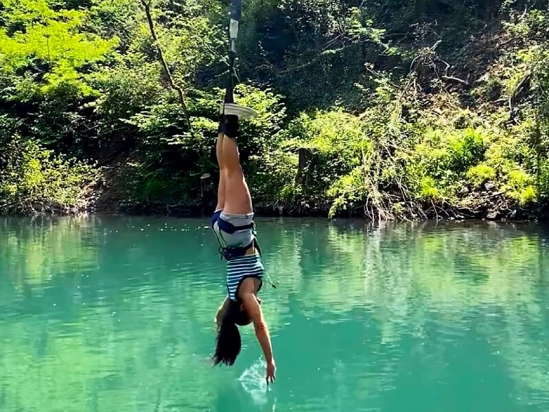 Femme suspendue à l'envers en saut à l'élastique au-dessus d'une eau claire et turquoise.