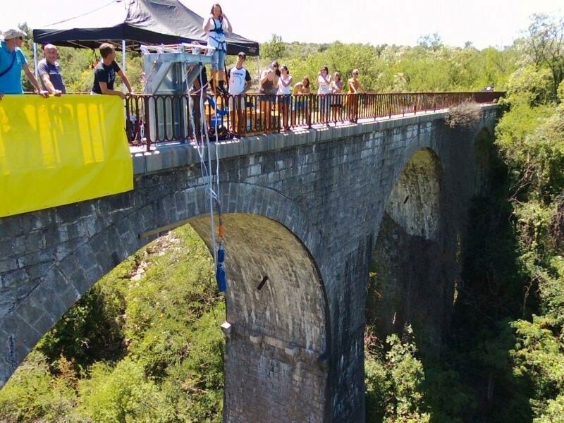 Groupe de personnes sur une plateforme de saut à l'élastique, préparant un participant pour le saut depuis un viaduc, tandis que d'autres observent l'événement depuis la rambarde