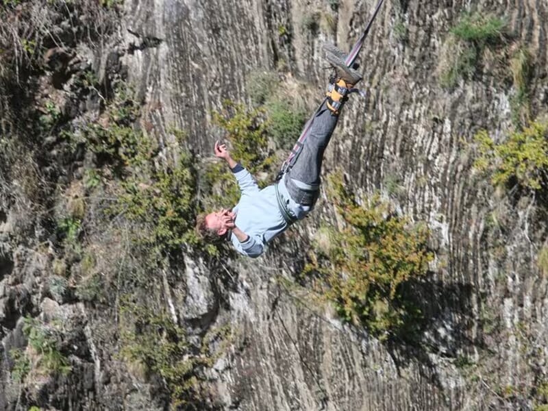 Homme en chute libre tête en bas, attaché par les chevilles pour un saut à l’élastique au-dessus d’une paroi rocheuse.