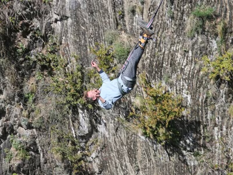 Homme en chute libre tête en bas, attaché par les chevilles pour un saut à l’élastique au-dessus d’une paroi rocheuse.