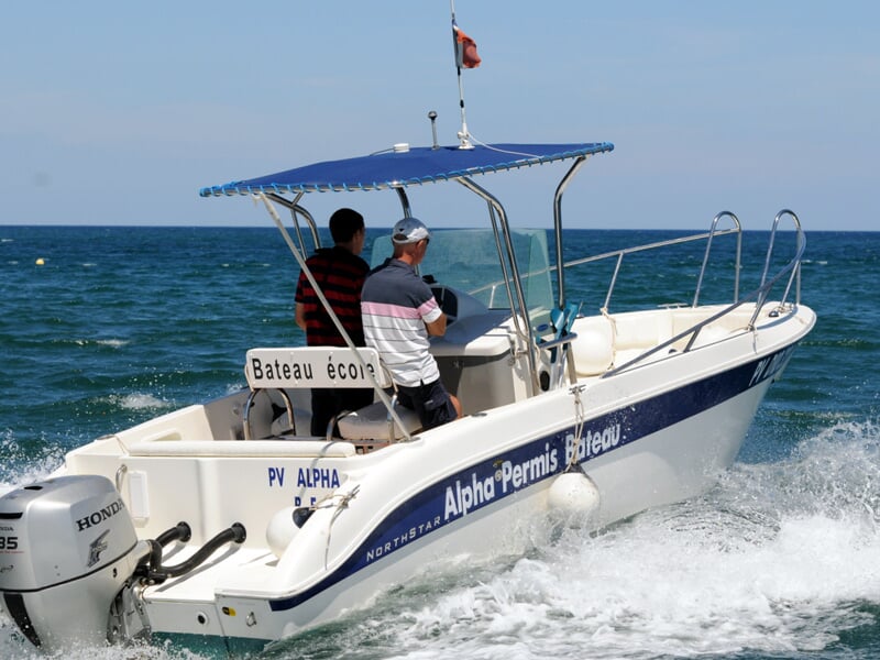 Deux personnes naviguent sur un bateau blanc avec un toit bleu sur une mer calme sous un ciel clair.