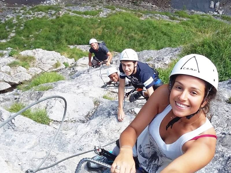 Groupe de personnes en casque et harnais souriants lors d'une activité de via ferrata en montagne.