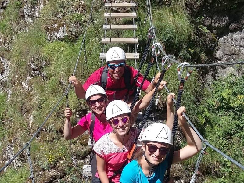 Quatre personnes en casque traversent un pont suspendu en bois lors d'une via ferrata en pleine nature.