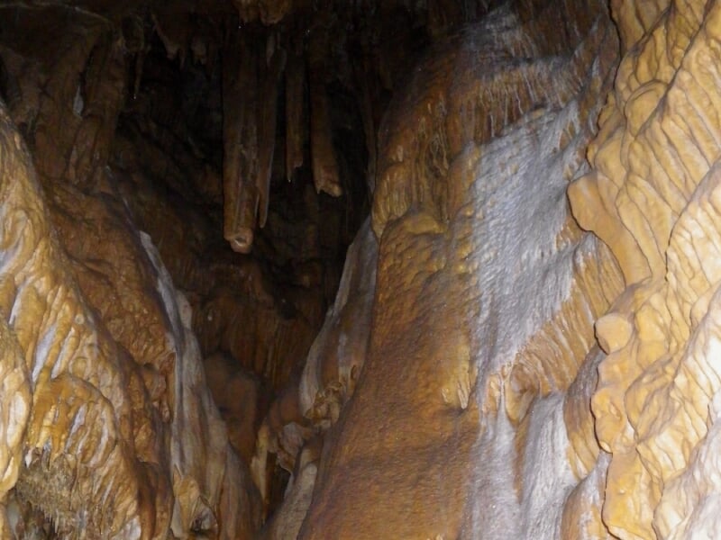 Intérieur d'une grotte avec stalactites et stalagmites aux formes naturelles, éclairé par une lampe frontale.