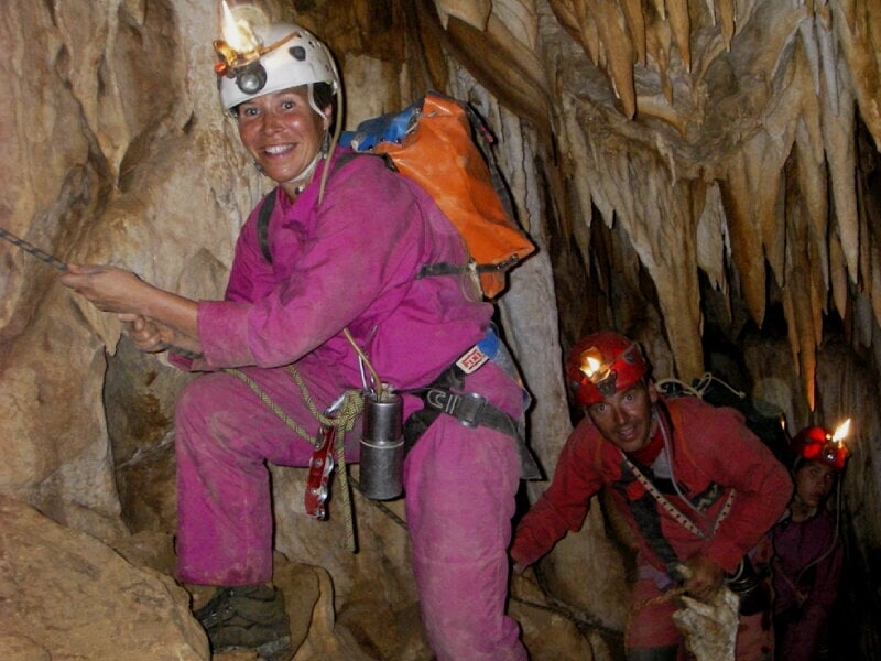 Groupe de spéléologues en combinaison colorée et casque rouge explorant une grotte aux parois rocheuses étroites.