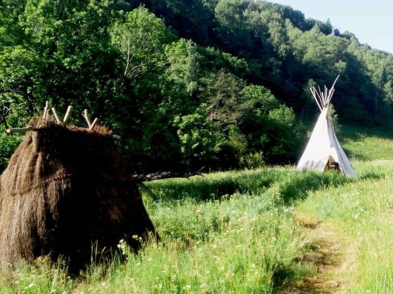 Intérieur d'un tipi avec des peaux d'animaux, des outils et des objets traditionnels suspendus et posés au sol.