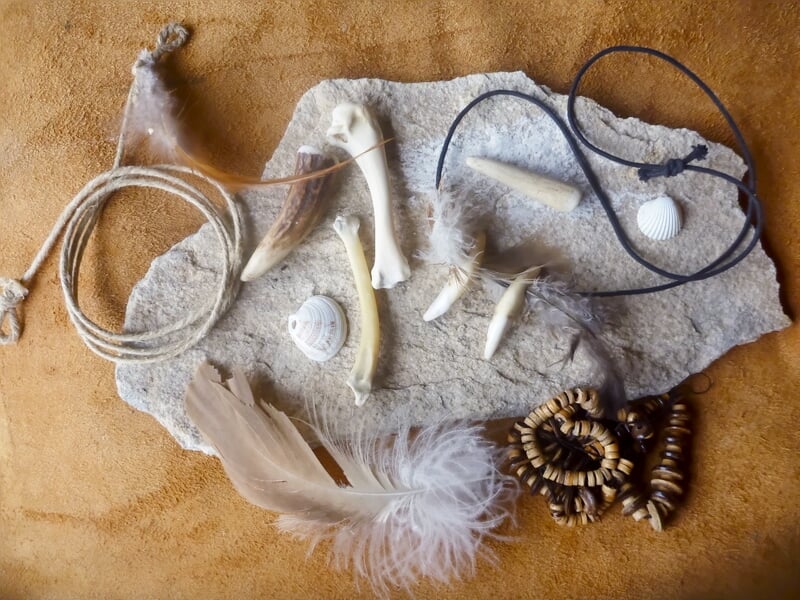 Divers outils et objets taillés en pierre et os, disposés sur un tissu marron dans un cadre naturel.