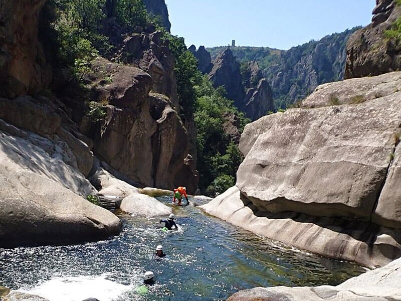 Personnes pratiquant le canyoning dans un canyon rocheux avec eau claire et paysage montagneux en arrière-plan.