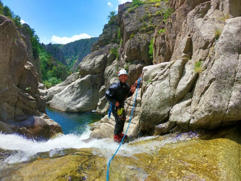 Homme équipé d'un casque et d'un harnais descend une cascade en rappel lors d'une activité de canyoning.