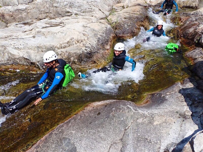 Trois personnes glissant sur un toboggan naturel en roche lors d'une descente de canyoning en rivière.