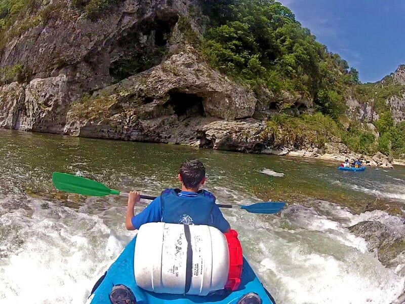 Vue depuis un kayak gonflable sur une rivière entourée de falaises et de végétation dense.