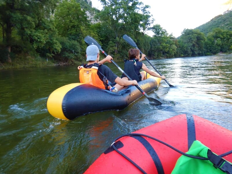 Deux personnes pagayant ensemble dans un kayak gonflable jaune et noir sur une rivière calme.