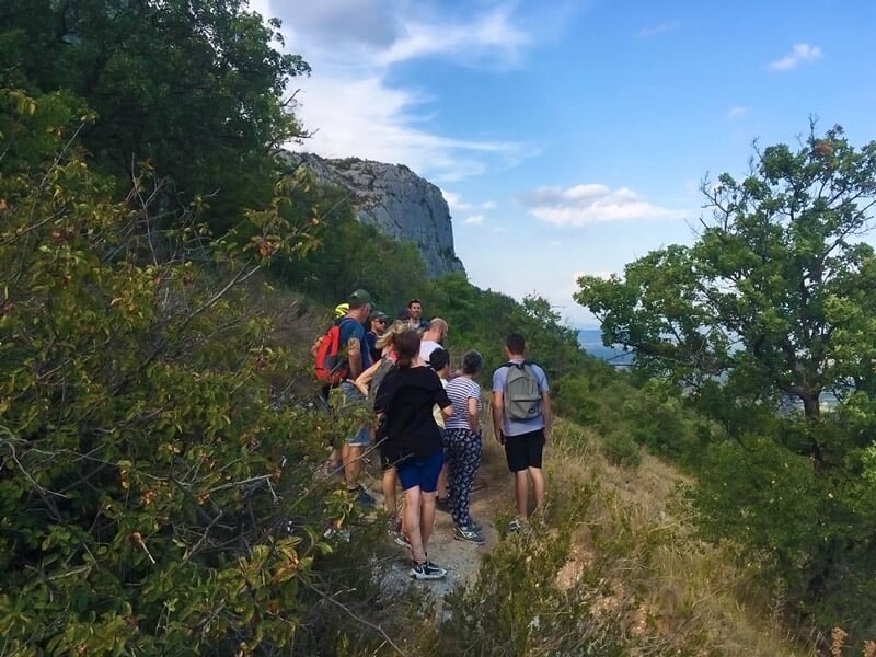Groupe de randonneurs marchant sur un sentier étroit en pleine nature avec vue sur la vallée.