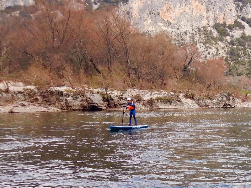 Deux personnes pratiquant le stand-up paddle sur une rivière calme entourée de falaises rocheuses.