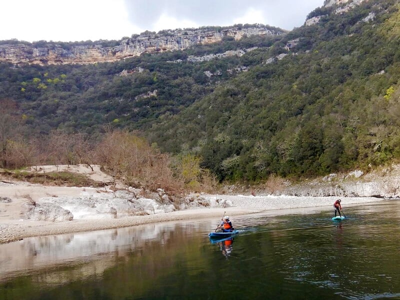 Deux personnes pagayant sur des planches de stand-up paddle sur une rivière entourée de nature.