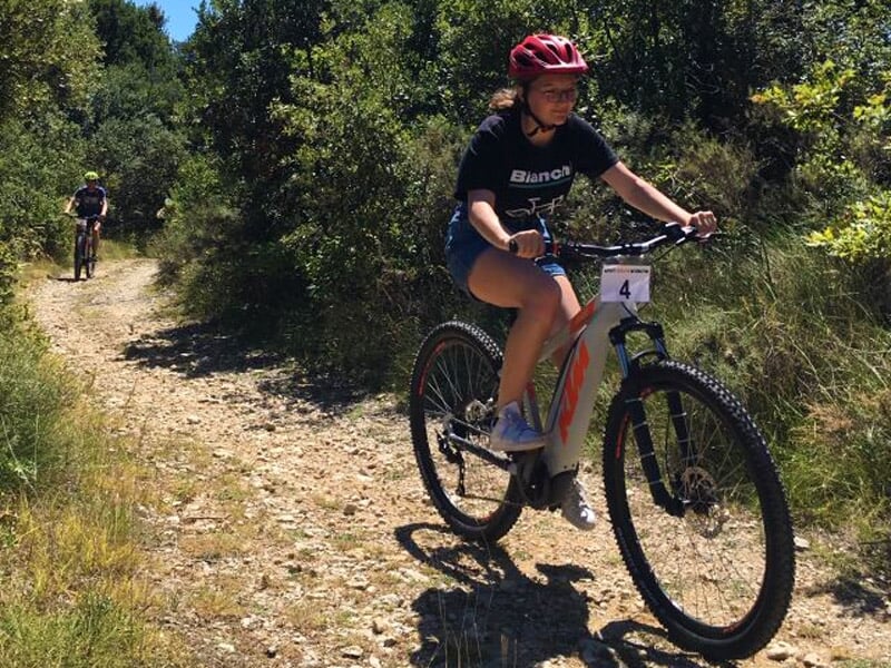 Jeune femme portant un casque roulant à vélo électrique sur un chemin de terre en pleine nature.