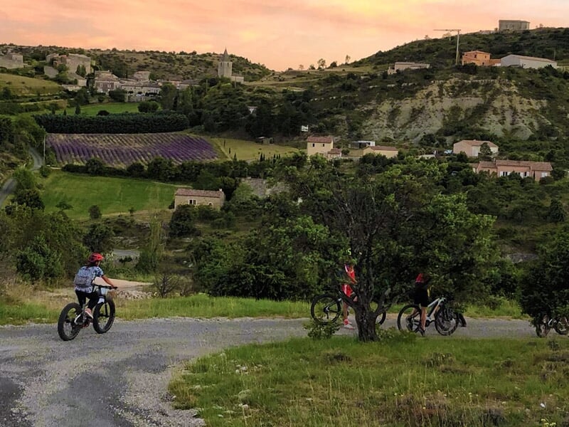 Cyclistes roulant sur une route de campagne au coucher du soleil avec des collines en arrière-plan.