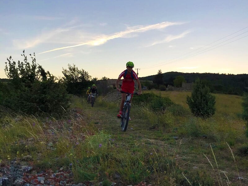 Personne roulant à vélo électrique sur un sentier herbeux entouré de collines et de végétation.