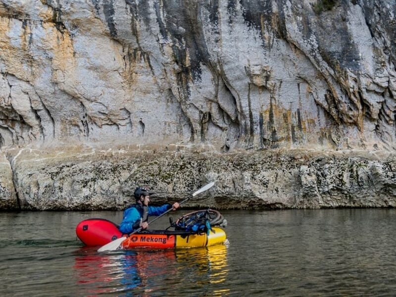 Kayakiste en kayak rouge et jaune pagayant près d'une falaise rocheuse lors d'une activité packraft à Vallon-Pont-D'Arc.
