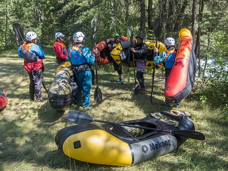Groupe de personnes en tenue de rafting avec casques, debout près de kayaks gonflables lors d'une activité packraft à Vallon-Pont-D'Arc.