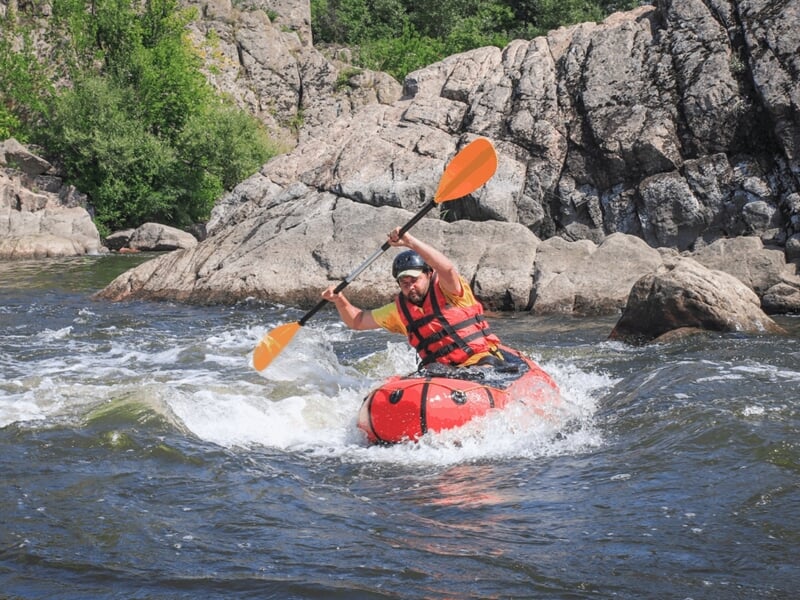Personne en kayak rouge pagayant vigoureusement dans une rivière lors d'une activité packraft à Vallon-Pont-D'Arc.