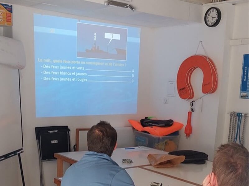 Salle de formation nautique avec un vidéoprojecteur affichant un quiz sur les feux de navigation.