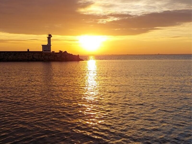Coucher de soleil sur la mer avec un phare sur une jetée rocheuse.
